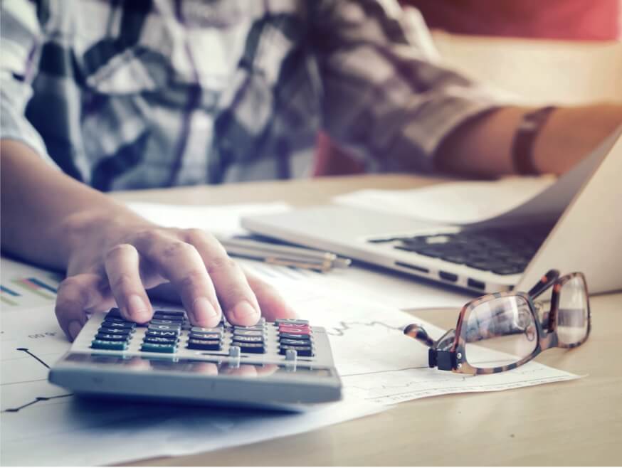 Close-up of a person with a calculator and laptop and papers with charts on them.